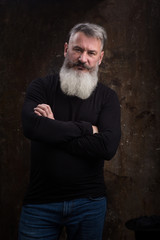 Studio portrait of handsome mature gray-haired bearded man against the dark wall, selective focus