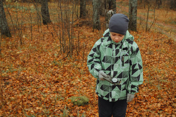 A teenage boy is guided by a compass in the woods. It's raining. Autumn.