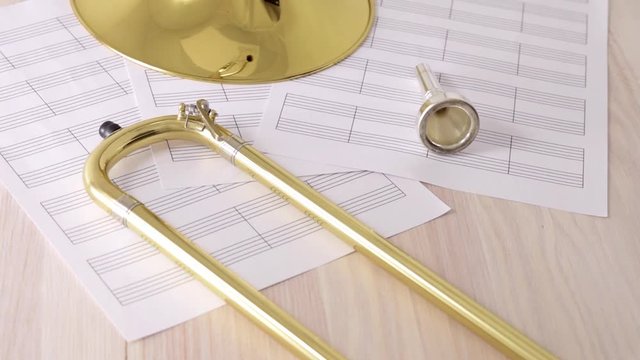 Disassembled golden trombone and scores on wooden table rotating view