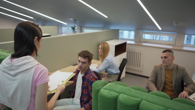 Displeased female manager walking down office corridor, entering cubicle and reproaching male employee working at desk. Manager dismissing worker and asking him to leave office
