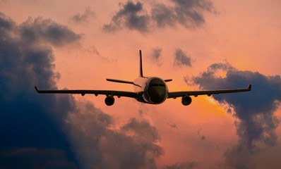Silhouette of commercial airplane jetliner flying above dramatic clouds in beautiful sunset light. Travel concept.
