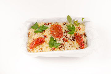 millet with sun-dried tomatoes and greens in container isolated on white background