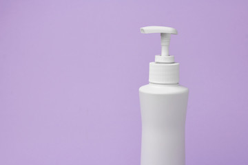 Mock up of white bottle with a dispenser on a purple background. Cosmetics packaging. Copy space for advertisement for cosmetic product.