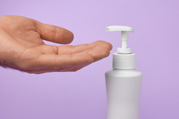 Closeup mans hand using antibacterial liquid soap to protect against COVID-19. Man uses gel for cleaning hands on a blue background.