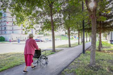 Elderly caucasian woman pushing wheelchair down a walking path