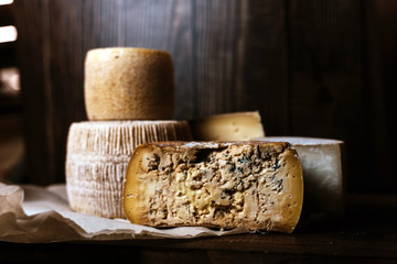 Different homemade cheeses on a dark wooden background. Pieces and cheese heads of Gorgonzola, Asiago, Maasdam, Gauda, Paramezan and Edam. Goat and cow cheese on baking paper. Handwork. Close up