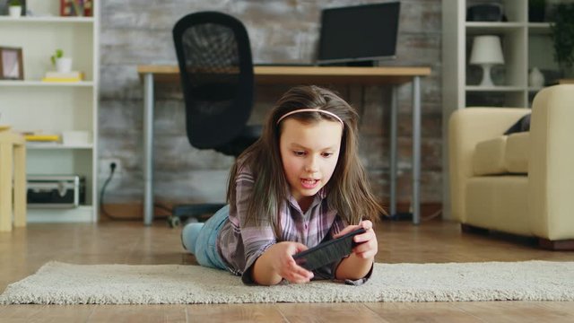 Cheerful little girl lying down on the floor playing video games