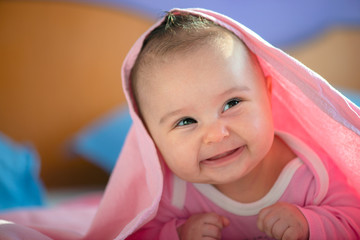 Cute three months old Baby girl infant on a bed on her belly with head up looking into camera with her big eyes. Natural bedroom light.