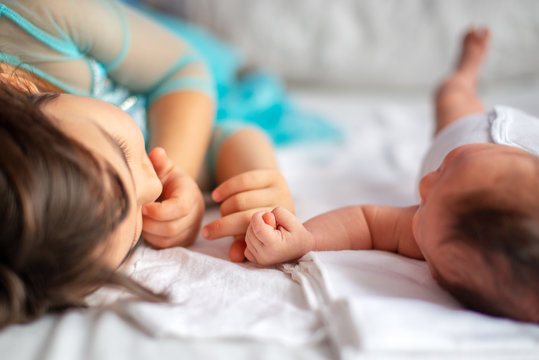 newborn baby with her older sister together on the bed holding each other`s hand