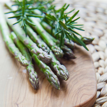 Green sparagus veg on the wooden board, decorated with fresh rosemary herb.