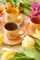 spring tea party. A bouquet of pastel tulips of different colors, small colorful cups on light background. Vertical image