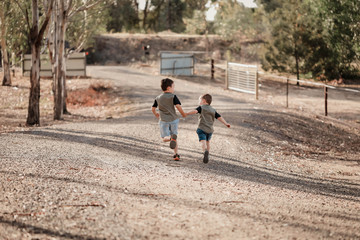 Two little brothers running away from camera along a bush track holding hands