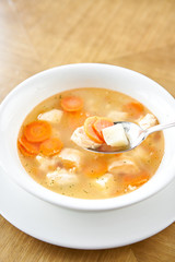 Fish soup in a white plate. Fish soup with vegetables, celery in a cup for the broth. Pike perch and salmon. Plate on wooden table. Restaurant menu