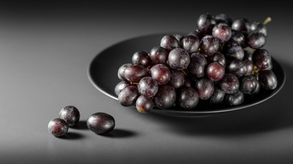 A bunch of ripe black grapes on a plate on a dark gray background.