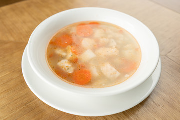 Fish soup in a white plate. Fish soup with vegetables, celery in a cup for the broth. Pike perch and salmon. Plate on wooden table. Restaurant menu