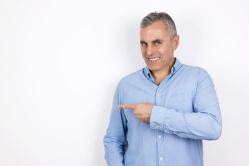 Fototapeta premium mature handsome man with grey hair wearing blue shirt standing on isolated white background points with his finger, body language concept