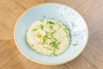 Mashed potatoes with dill in plate on a wooden background