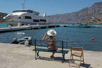 young girl in a white hat and a color summer dress on a bench. Bay promenade on a sunny day