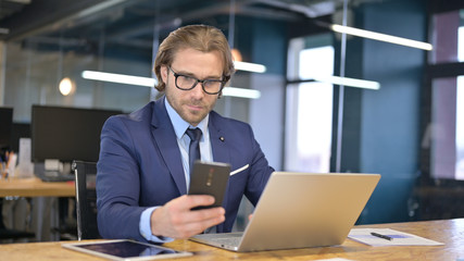 Businessman Using Smartphone and Laptop in Office