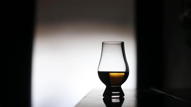 HD footage of a person putting  a Glencairn whisky glass on a table, backlit.