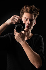 A beautiful young brunette in a dark jacket with a camera in his hands on a dark background