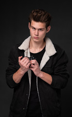 A beautiful young brunette in a dark jacket with a camera in his hands on a dark background