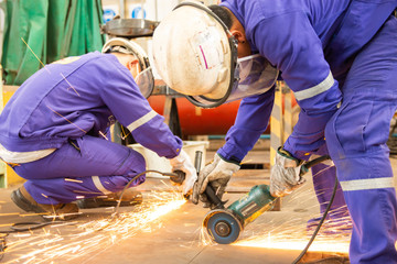 Two male workers cutting metal sheets with electric grider in the workshop.