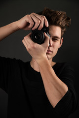 A beautiful young brunette in a dark jacket with a camera in his hands on a dark background