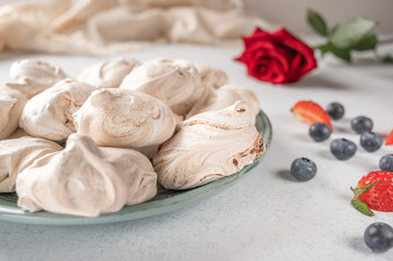 Homemade dessert meringue on a plate on white background. Napkin, strawberry and blueberry berries and red rose flower