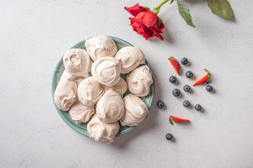 Homemade popular dessert meringue on a plate on white background. Nearby are strawberry and blueberry berries and red rose flower