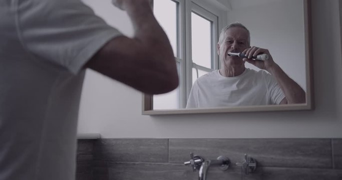 Senior adult male brushing teeth with electric toothbrush in bathroom in the morning