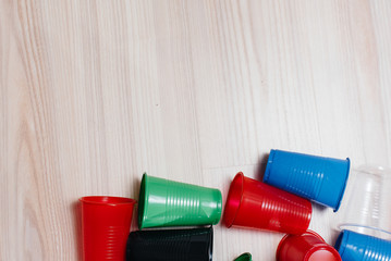 A large pile of multicolored plastic cups scattered on the floor with free space. Pollution of the environment by human waste