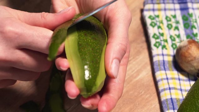 Cleansing the avocado from the peel with a silver knife, static close-up shot. Cooking guacamole in the kitchen, a woman holds a ripe avocado