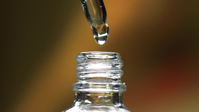 Close up macro of pipette with serum liquid drop in glass bottle. 4k slow motion footage of cosmetic health care or skin tone liquid.