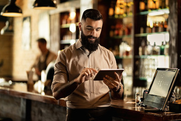 Smiling barista using digital tablet while working in a bar. - obrazy, fototapety, plakaty