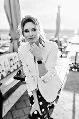 Рortrait of an attractive European girl  in a white blazer and culottes in peas posing near the table in a street cafe. Black and white photo. Soft focus.