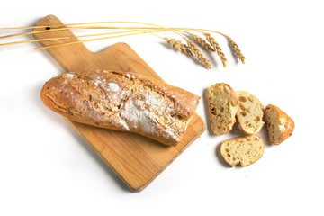Half sliced baguette or French bread baked with onions on a kitchen board and some wheat ears isolated with shadows on a white background, copy space, high angle view from above