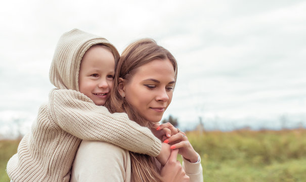 little boy hugs woman mom, autumn day on nature in field, warm beige sweater with hood. Emotions of care nurturing love and support. Free space for copy text. Happy smiling rejoices.