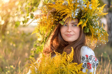 Young beautiful woman in a wreath of wildflowers and embroidered shirt outdoors on a sunny day. Close-up portrait