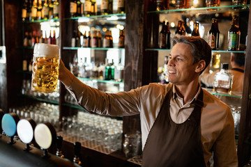Happy bartender with glass of draft beer in a bar.