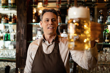 Happy mid adult barista with glass of beer in a pub.