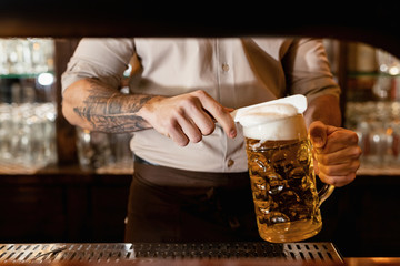 Unrecognizable barista removing beer froth while serving beer in a bar.