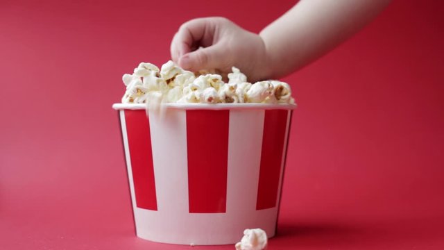 childrens Caucasian hand taking popcorn from striped red and white paper box