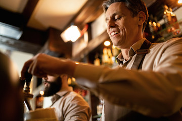 Below view of happy bartender pouring beer form beer tap in a bar.