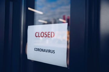 Woman hangs a card with information about the store closing on a shop window due to the coronavirus