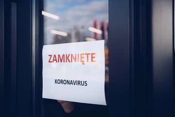 Woman hangs a card with information about the store closing on a shop window due to the coronavirus...