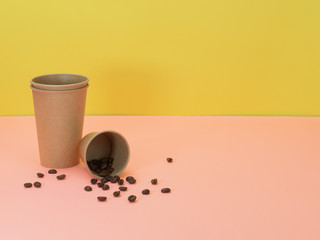 Paper cups and coffee beans on pink and yellow background.