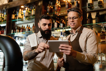 Two bartenders using digital tablet while working in a bar.