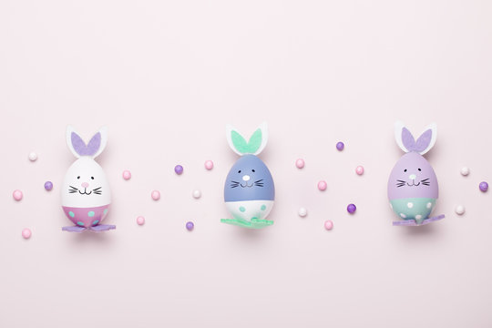 Funny cute bunny eggs in pastel colors on pink table top, Easter holiday concept. Easter decoration for kids still life, copy space