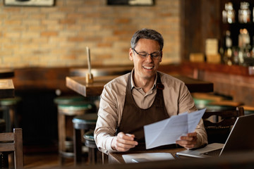Happy waiter working on paperwork after working hours in a pub.